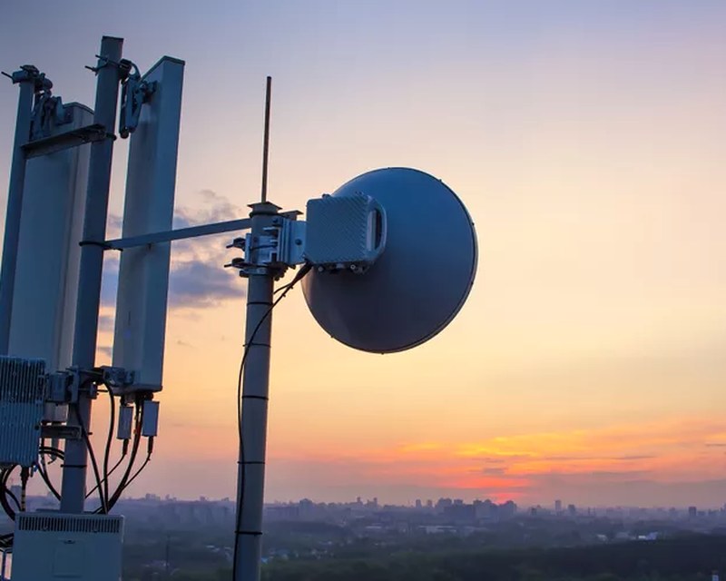 A cellular antenna and dish at sunset — predictive AI fixing the network before the ticket